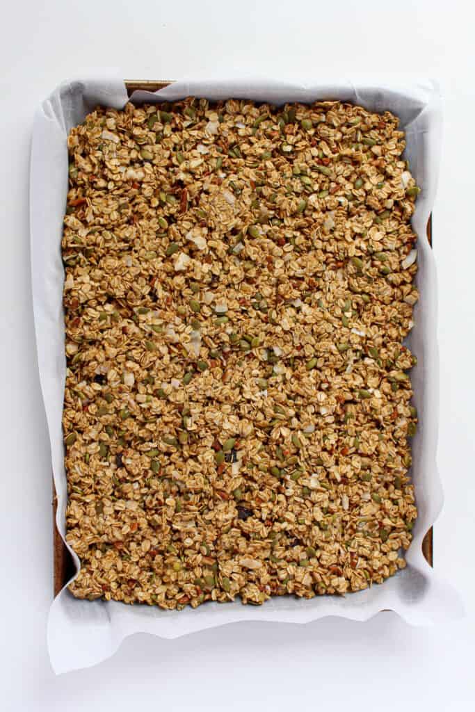 Pre-baked granola ingredients pressed down firmly on a large baking sheet that is lined with parchment paper