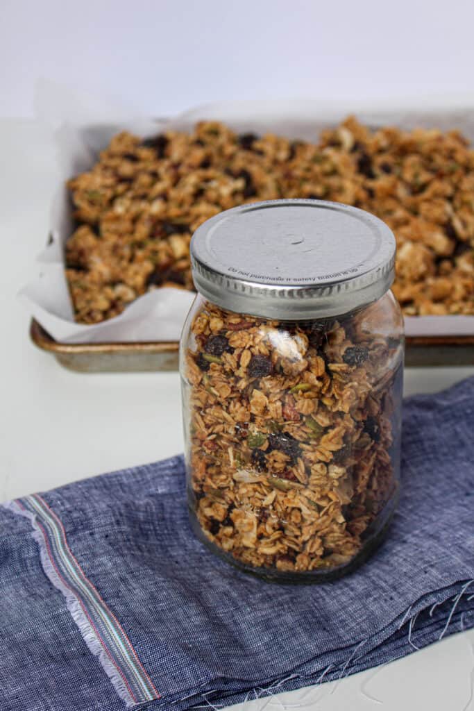 Jar of peanut butter granola in front of a baking sheet with granola on it.