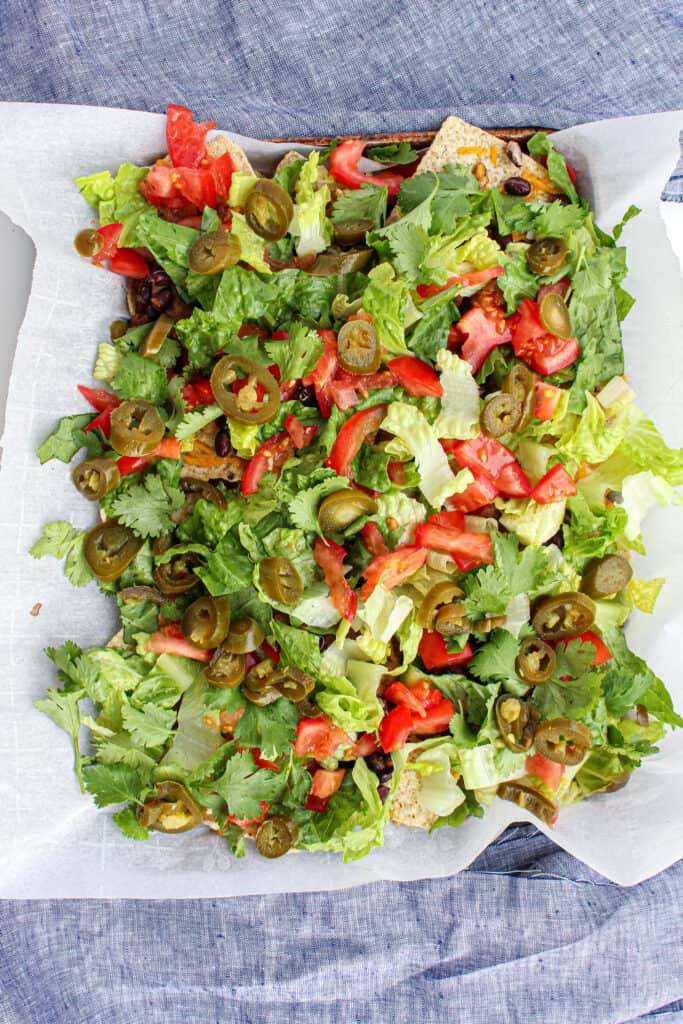 above view of a sheet pan of nachos covered with lettuce, pickled jalapeno, and tomatoes