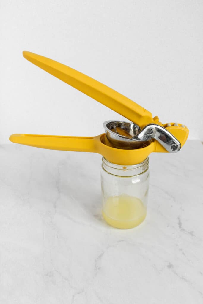 A lemon squeezer (also called a citrus juicer) sitting on top of a glass jar with freshly squeezed lemon juice in it.