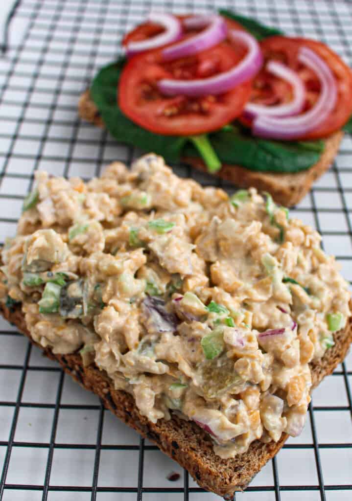 Open-face vegan chickpea tuna salad sandwich with spinach, sliced tomato, and red onion