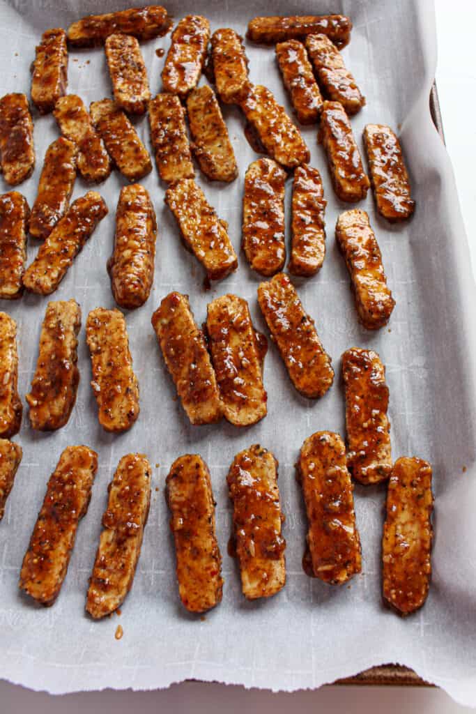 Thinly sliced marinated tempeh on parchment paper a baking sheet