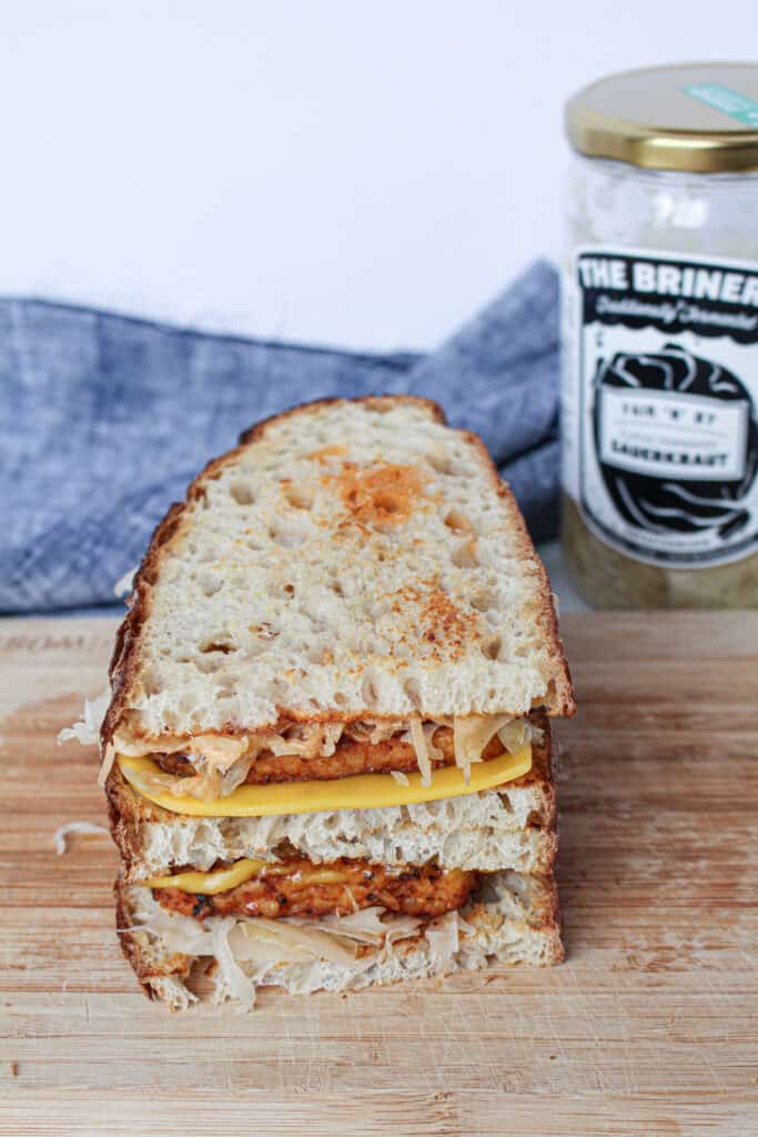 A ready-to-eat tempeh reuben sandwich with a jar of sauerkraut in the background  