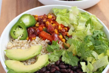 Two white bowls filled with rice, black beans, fiesta vegetables, lettuce, cilantro and pickled jalapeno on a wooden background