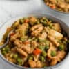 Two grey bowls filled with Vegan 'Chick'n' and Potato Soup with a white plate in the background with out of focus large carrots and celery.