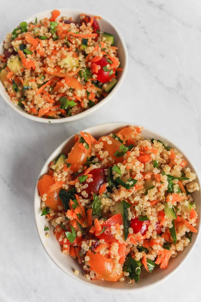 Two serving bowls filled with the quinoa tabbouleh salad on a marble background