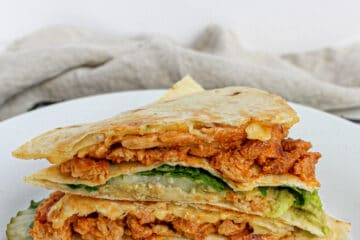 A stacked Vegan Buffalo Chick'n Wrap on a white plate with a tan cloth napkin in the background
