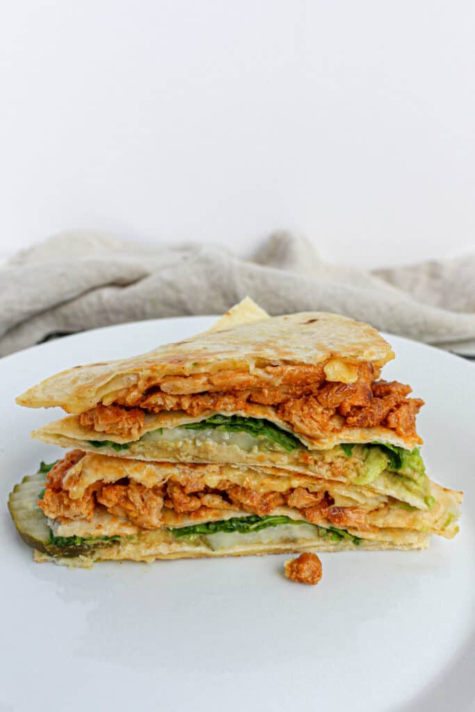 A stacked Vegan Buffalo Chick'n Wrap on a white plate with a tan cloth napkin in the background