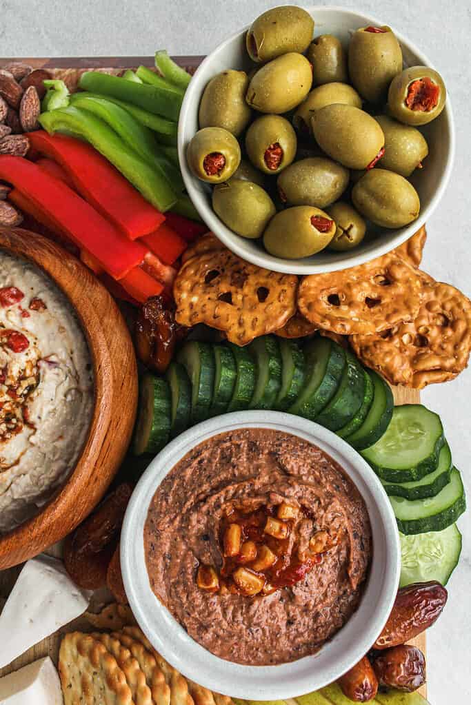 Up close view of upper lefthand corned of vegan snack board which includes green olives, bean dip cucmbers, dates, and crackers