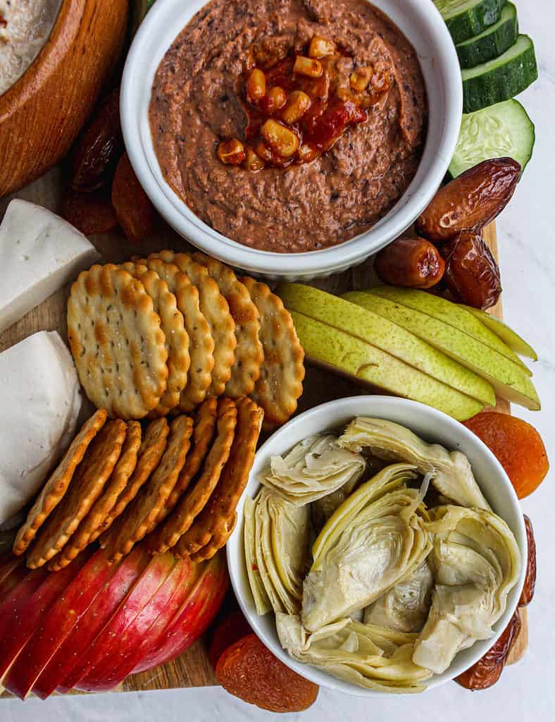Left lower corner of Vegan Charcuterie Board which includes artichokes, crackers, slices apples, pears, and apricots.