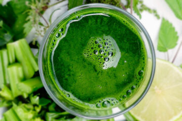 Glass filled with a green smoothie. Surrounded by celery, herbs and lemon.
