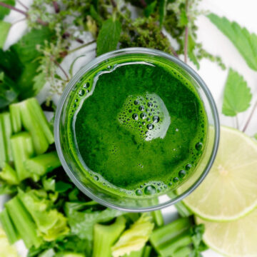 Glass filled with a green smoothie. Surrounded by celery, herbs and lemon.