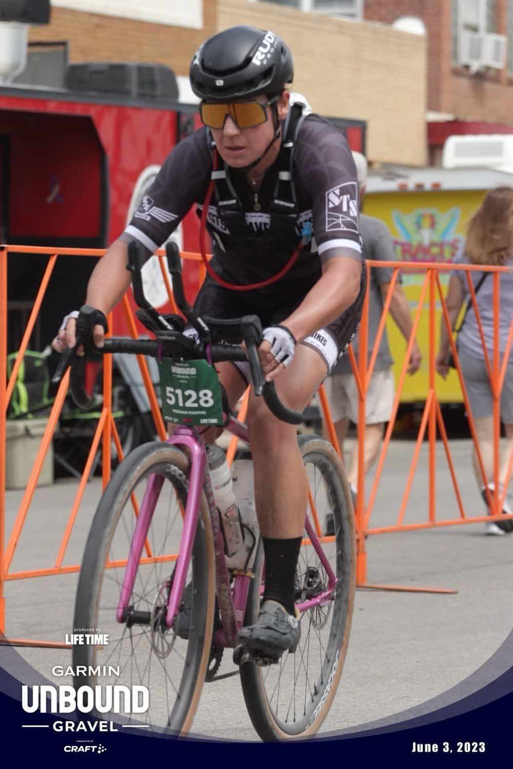 A white woman on a purple bike at race. She is wearing a black cycling kit.